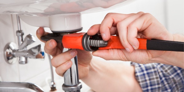 A plumber fixing the drain under a bathroom sink.